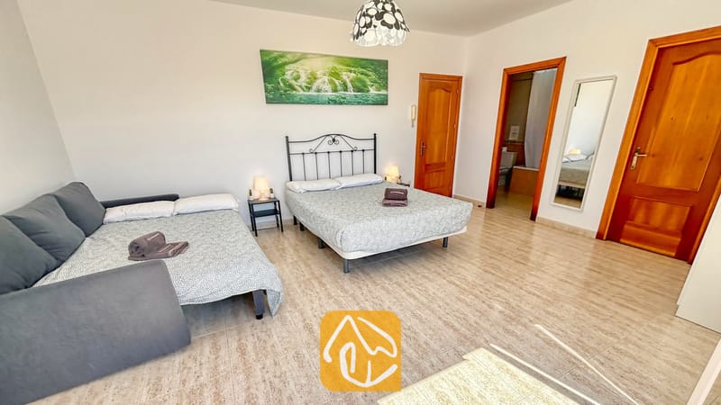 Villas de vacances Costa Brava Espagne - Villa Holiday - Spacieuse chambre à la Villa Holiday dotée d'un lit double avec un cadre en métal noir, d'un lit simple gigogne attenant, de sols en carrelage clair et de deux portes en bois.