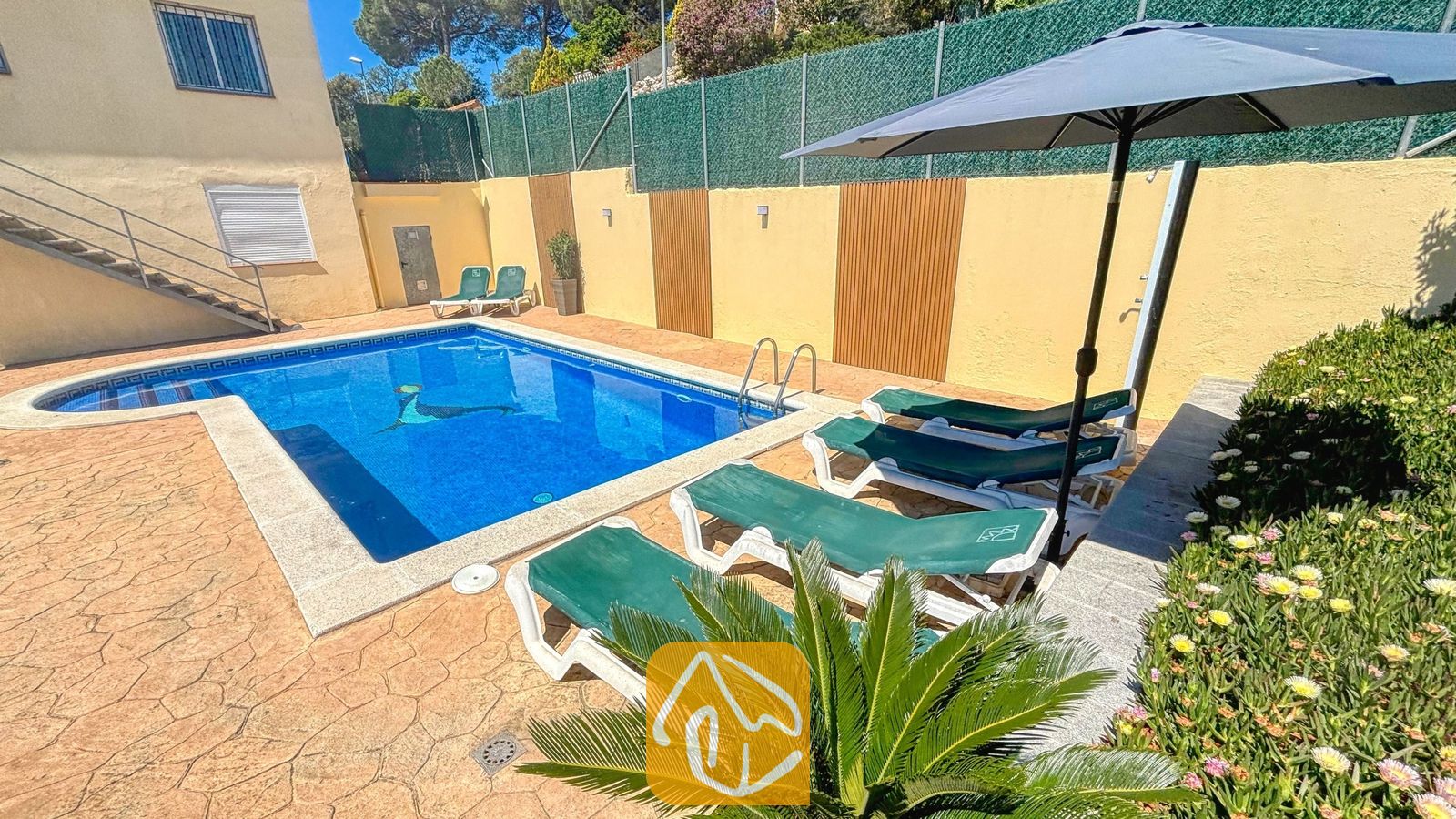 Vakantievilla's Costa Brava Spanje - Villa Holiday - Privé buitenzwembad bij Villa Holiday, omringd door groene ligbedden, een donkere parasol en een stenen terras.