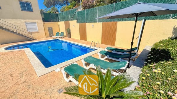 Vakantievilla's Costa Brava Spanje - Villa Holiday - Privé buitenzwembad bij Villa Holiday, omringd door groene ligbedden, een donkere parasol en een stenen terras.