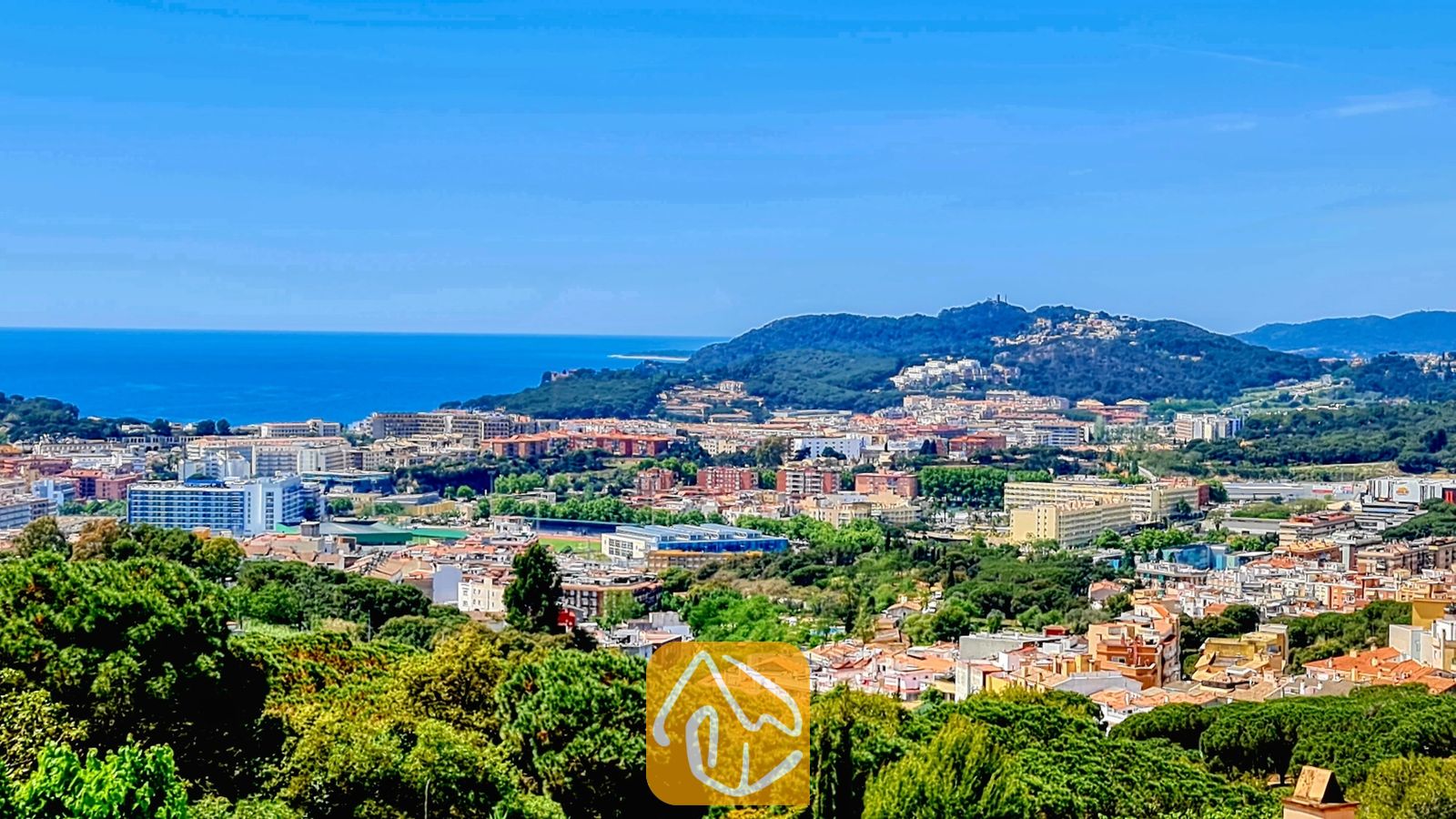 Vakantievilla's Costa Brava Spanje - Villa Maribel - Een verhoogd uitzicht vanuit Villa Maribel met uitzicht op een Spaans kuststadje, groene heuvels en de blauwe zee onder een heldere hemel.