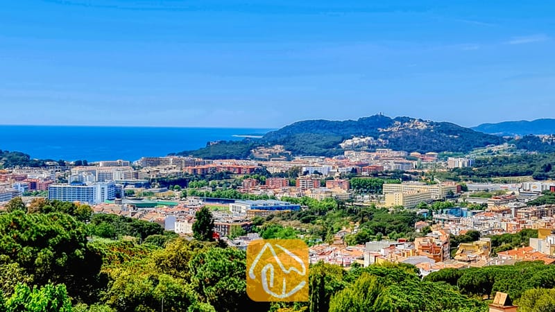 Vakantievilla's Costa Brava Spanje - Villa Maribel - Een verhoogd uitzicht vanuit Villa Maribel met uitzicht op een Spaans kuststadje, groene heuvels en de blauwe zee onder een heldere hemel.