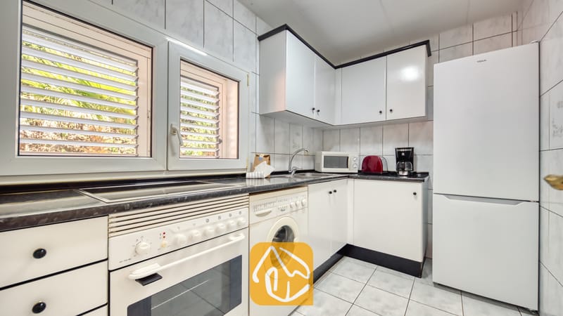 Vakantievilla's Costa Brava Spanje - Villa Maribel - Keuken met witte kasten, een ingebouwde oven, wasmachine en twee ramen met rolluiken aan de buitenzijde.