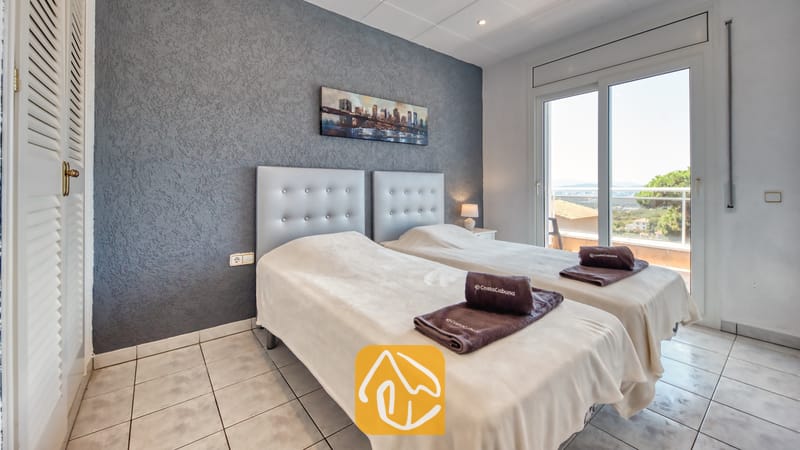 Vakantievilla's Costa Brava Spanje - Villa Maribel - Slaapkamer met twee eenpersoonsbedden tegen een getextureerde grijze wand, tegelvloer en schuifpui die toegang biedt tot een balkon.