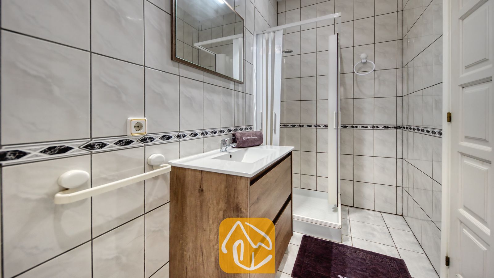 Vakantievilla's Costa Brava Spanje - Villa Maribel - Badkamer met een houten badkamermeubel, een wit keramische wastafel, een spiegel en een inloopdouche met tegelmuren.