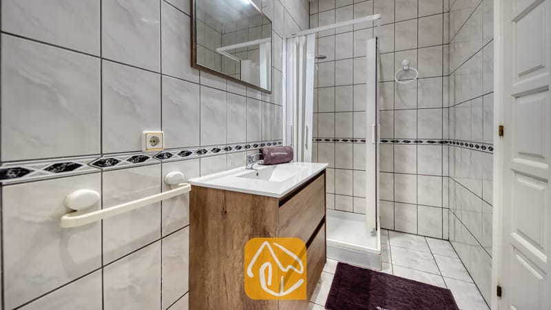 Vakantievilla's Costa Brava Spanje - Villa Maribel - Badkamer met een houten badkamermeubel, een wit keramische wastafel, een spiegel en een inloopdouche met tegelmuren.