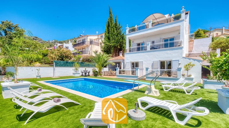 Vakantievilla's Costa Brava Spanje - Villa Maribel - Buitenaanzicht van Villa Maribel met een rechthoekig zwembad, een duikplank en witte ligstoelen op een groen kunstgrasveld tegen een helderblauwe hemel.
