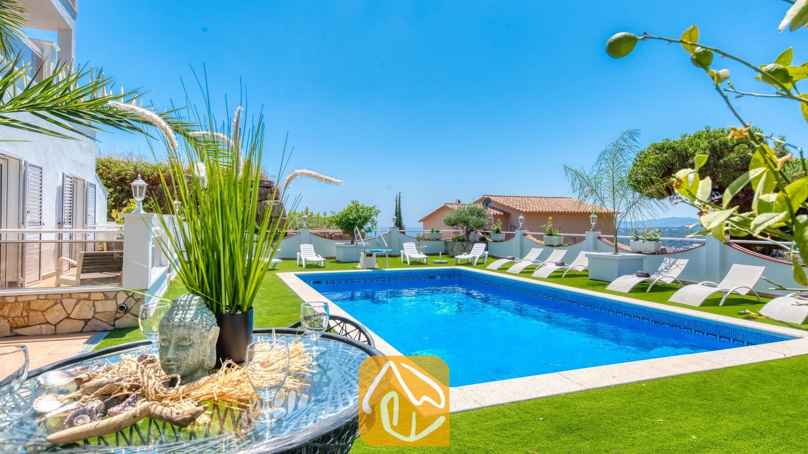 Vakantievilla's Costa Brava Spanje - Villa Maribel - Privézwembad en terras bij Villa Maribel, voorzien van kunstgras, witte ligstoelen en een glazen tafel met decoratieve ornamenten.