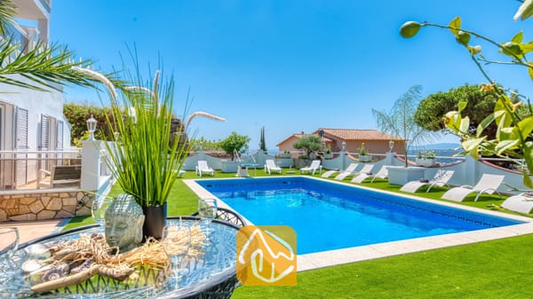 Vakantievilla's Costa Brava Spanje - Villa Maribel - Privézwembad en terras bij Villa Maribel, voorzien van kunstgras, witte ligstoelen en een glazen tafel met decoratieve ornamenten.