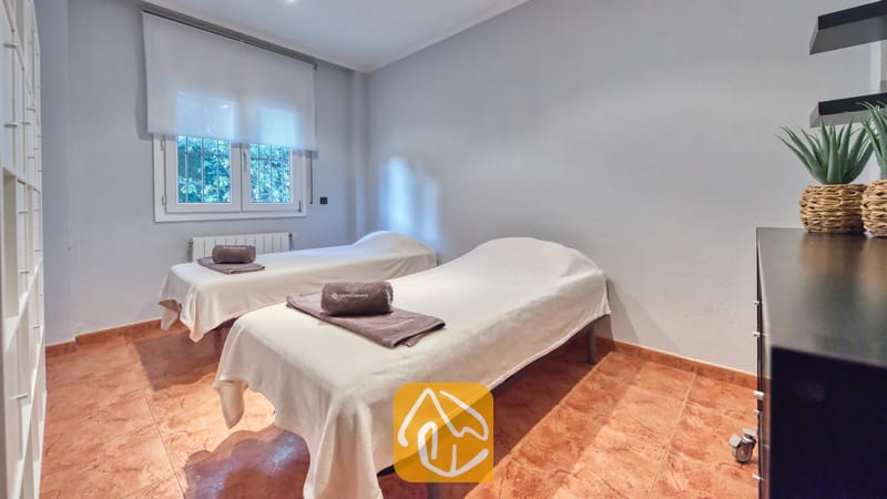 Vakantievilla's Costa Brava Spanje - Villa Summertime - Massagekamer met twee behandelbedden voorzien van witte lakens, elk met een opgevouwen grijze handdoek erop, tegelvloer en een raam met een wit rolgordijn.