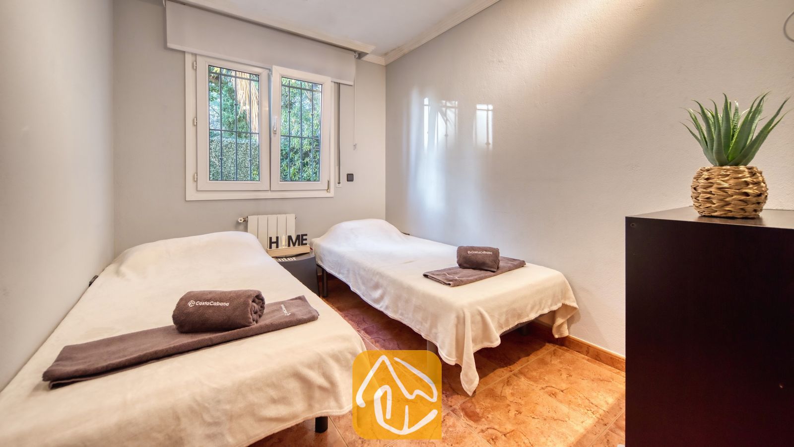 Vakantievilla's Costa Brava Spanje - Villa Summertime - Tweepersoonskamer met twee eenpersoonsbedden voorzien van witte spreuken en opgevouwen bruine handdoeken, tegelvloer en een klein raam met uitzicht op groen.