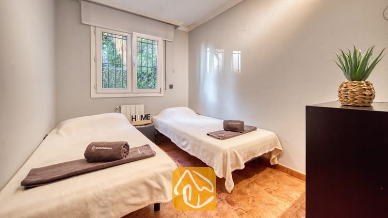 Vakantievilla's Costa Brava Spanje - Villa Summertime - Tweepersoonskamer met twee eenpersoonsbedden voorzien van witte spreuken en opgevouwen bruine handdoeken, tegelvloer en een klein raam met uitzicht op groen.