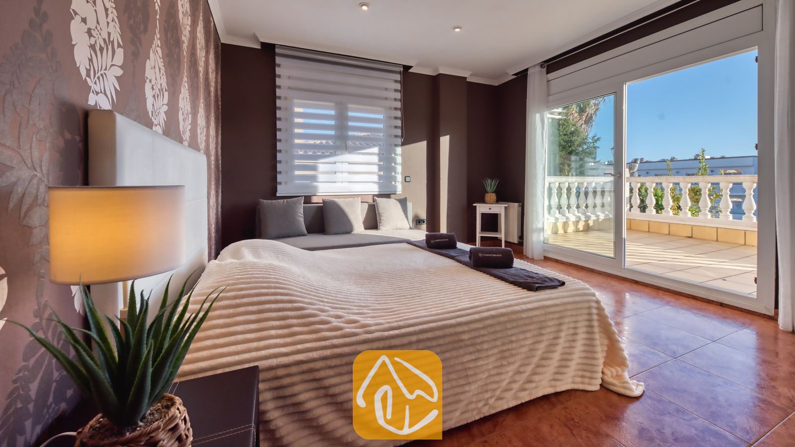 Vakantievilla's Costa Brava Spanje - Villa Summertime - Slaapkamer met een tweepersoonsbed, donkerbruine muren, gedessineerd behang en glazen schuifdeuren die uitkomen op een zonnig balkon bij Villa Summertime.