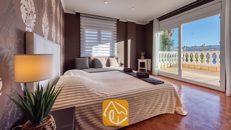 Vakantievilla's Costa Brava Spanje - Villa Summertime - Slaapkamer met een tweepersoonsbed, donkerbruine muren, gedessineerd behang en glazen schuifdeuren die uitkomen op een zonnig balkon bij Villa Summertime.