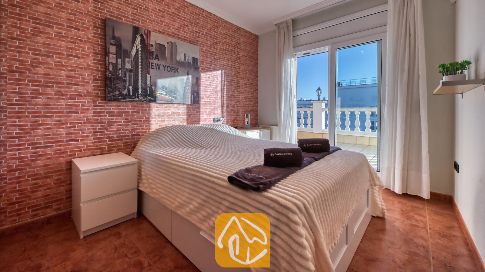 Vakantievilla's Costa Brava Spanje - Villa Summertime - Slaapkamer met een tweepersoonsbed, een karakteristieke muur van rode baksteen, muurdecoratie van de skyline van New York en schuifpui die toegang biedt tot een balkon.