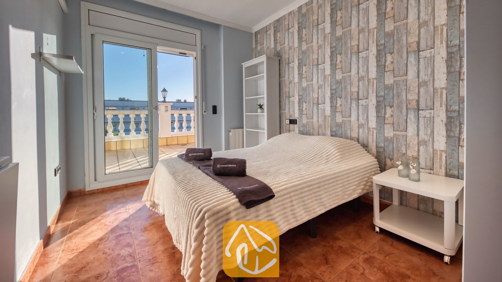 Vakantievilla's Costa Brava Spanje - Villa Summertime - Slaapkamer met een tweepersoonsbed, een witte, getextureerde sprei en open glazen deuren die leiden naar een lichte buitenterras.