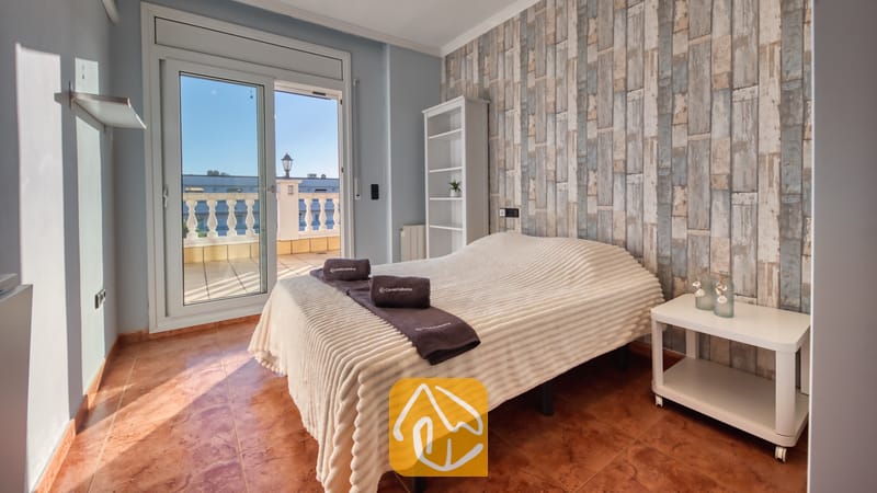 Vakantievilla's Costa Brava Spanje - Villa Summertime - Slaapkamer met een tweepersoonsbed, een witte, getextureerde sprei en open glazen deuren die leiden naar een lichte buitenterras.
