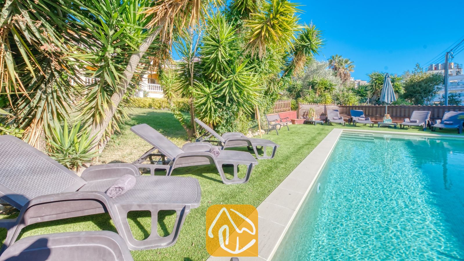 Vakantievilla's Costa Brava Spanje - Villa Summertime - Privé-buitenzwembad bij Villa Summertime, omringd door een groen gazon, grijskunststof ligstoelen en tropische palmbomen onder een blauwe lucht.