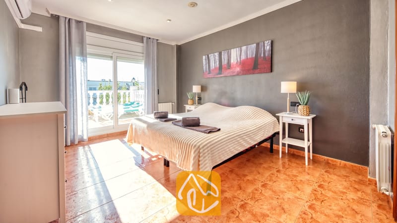Vakantievilla's Costa Brava Spanje - Villa Summertime - Slaapkamer met een tweepersoonsbed, witte nachtkastjes met lampen, donkergrijze muren, tegelvloer en een schuifpui die toegang biedt tot een balkon.