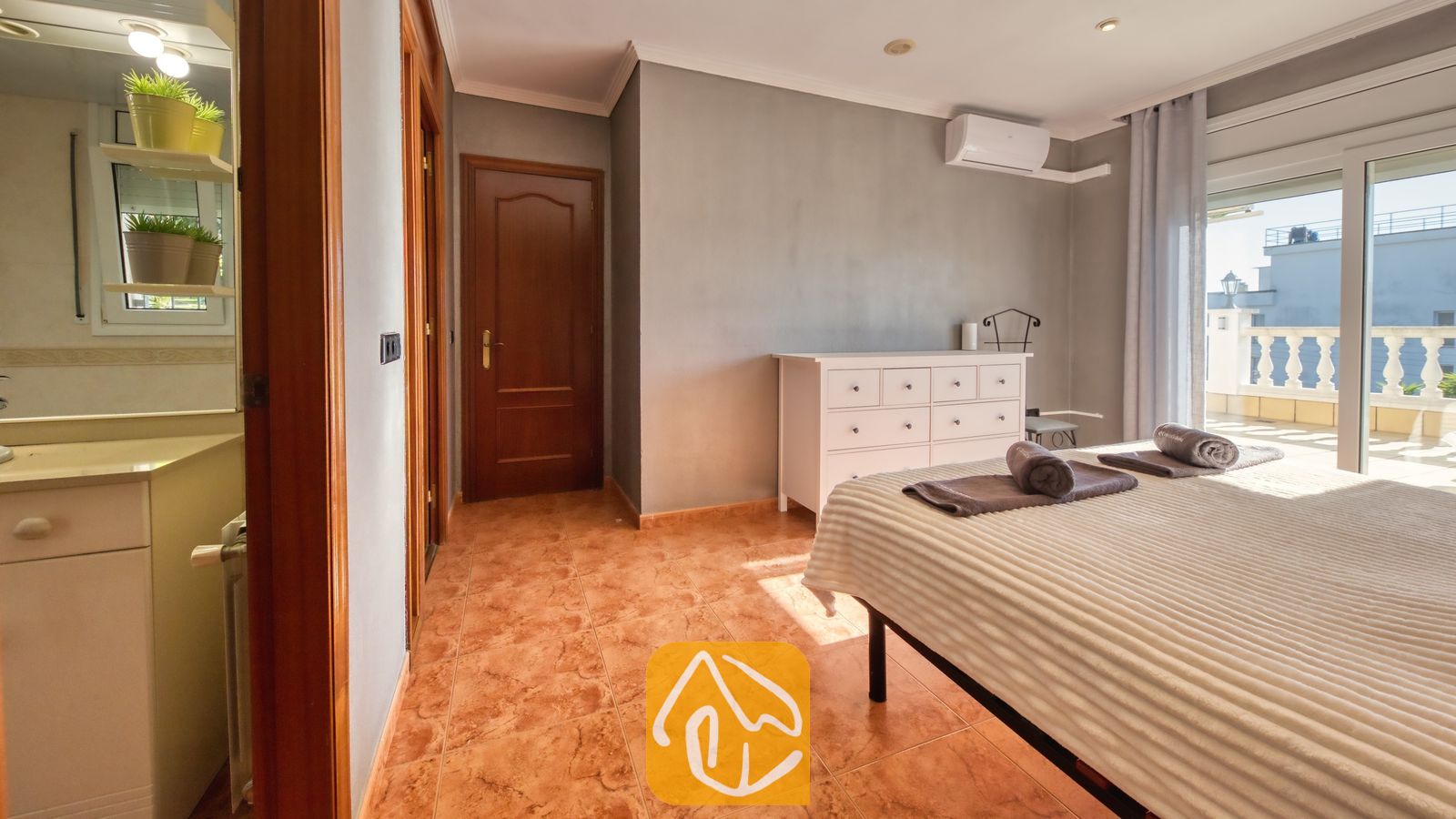 Vakantievilla's Costa Brava Spanje - Villa Summertime - Slaapkamer met grijze muren, tegelvloeren, een witte commode en glazen schuifpui die toegang biedt tot een lichte balkon.