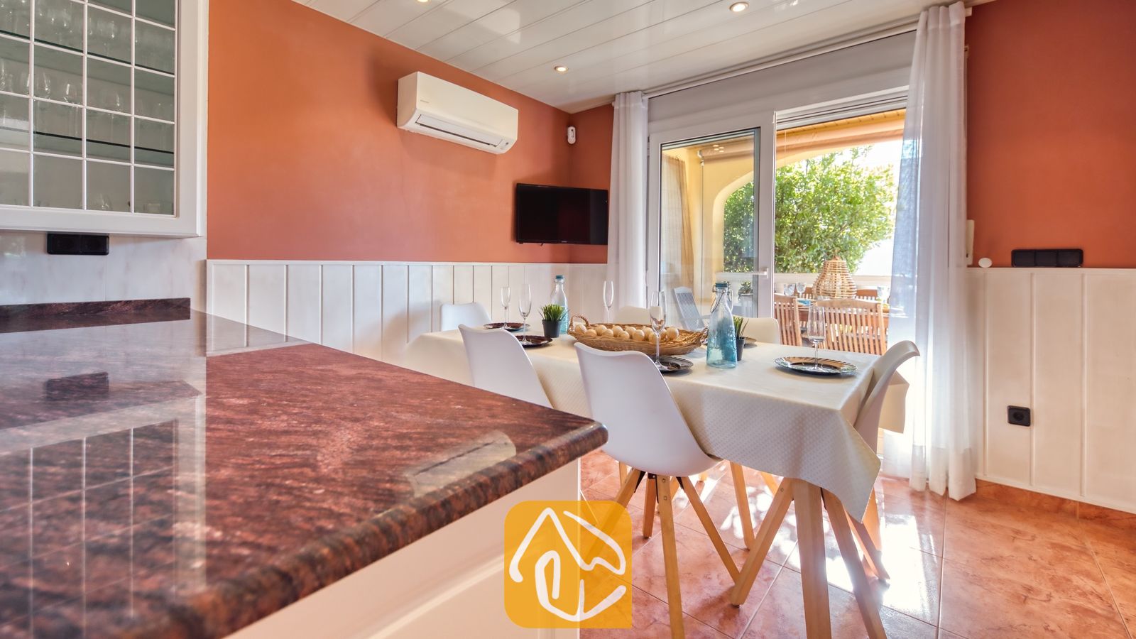 Vakantievilla's Costa Brava Spanje - Villa Summertime - Eethoek binnen in Villa Summertime, voorzien van een houten tafel met witte stoelen, terracotta plavuizen en glazen schuifdeuren die openen naar een terras.