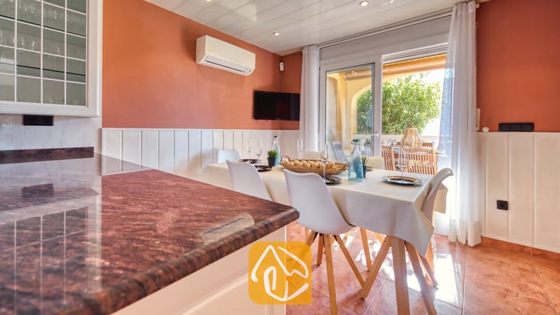 Vakantievilla's Costa Brava Spanje - Villa Summertime - Eethoek binnen in Villa Summertime, voorzien van een houten tafel met witte stoelen, terracotta plavuizen en glazen schuifdeuren die openen naar een terras.