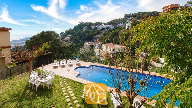 Vakantievilla's Costa Brava Spanje - Villa Marysol - Villa Marysol beschikt over een buitenzwembad omringd door witte ligstoelen, een eettafel op het grasveld en een bergdorpje op de achtergrond.