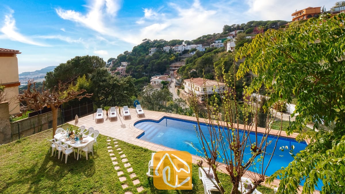 Vakantievilla's Costa Brava Spanje - Villa Marysol - Villa Marysol beschikt over een buitenzwembad omringd door witte ligstoelen, een eettafel op het grasveld en een bergdorpje op de achtergrond.