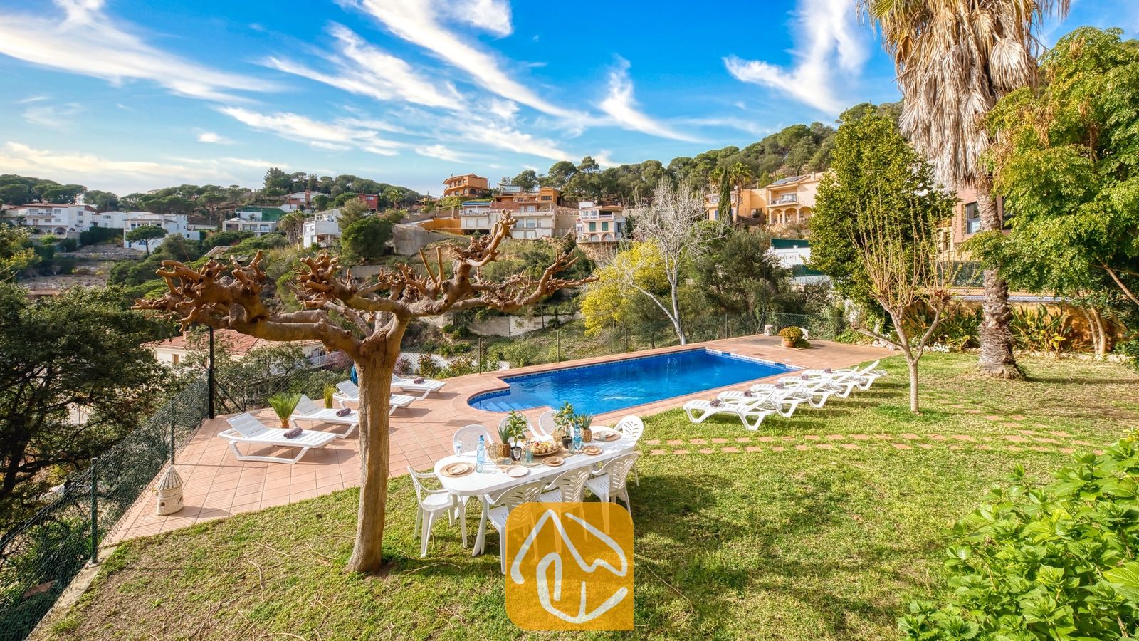 Vakantievilla's Costa Brava Spanje - Villa Marysol - Privézwembad bij Villa Marysol, omringd door een betegeld terras, een grasveld, een eettafel met stoelen en ligstoelen, met een achtergrond van glooiende heuvels