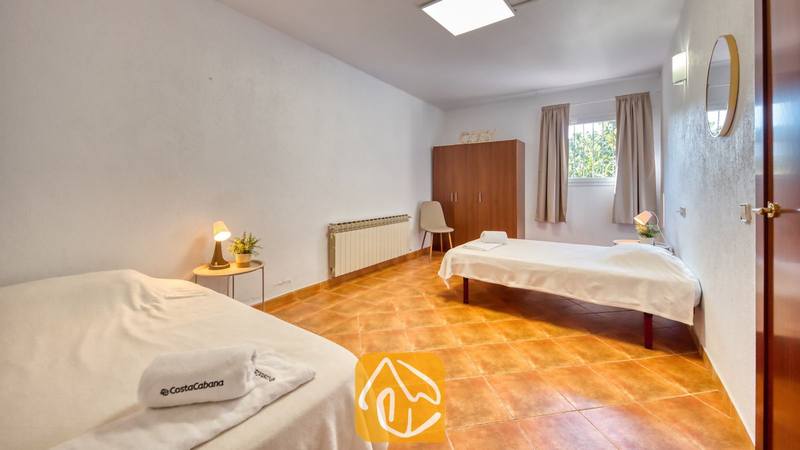 Vakantievilla's Costa Brava Spanje - Villa Marysol - Slaapkamer met twee eenpersoonsbedden voorzien van wit beddengoed, een houten kledingkast, oranje tegelvloer en een klein nachtkastje met een lamp.