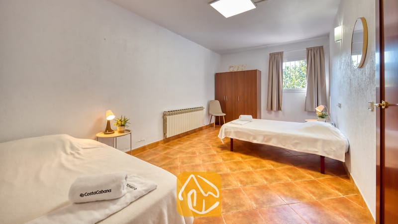 Vakantievilla's Costa Brava Spanje - Villa Marysol - Slaapkamer met twee eenpersoonsbedden voorzien van wit beddengoed, een houten kledingkast, oranje tegelvloer en een klein nachtkastje met een lamp.