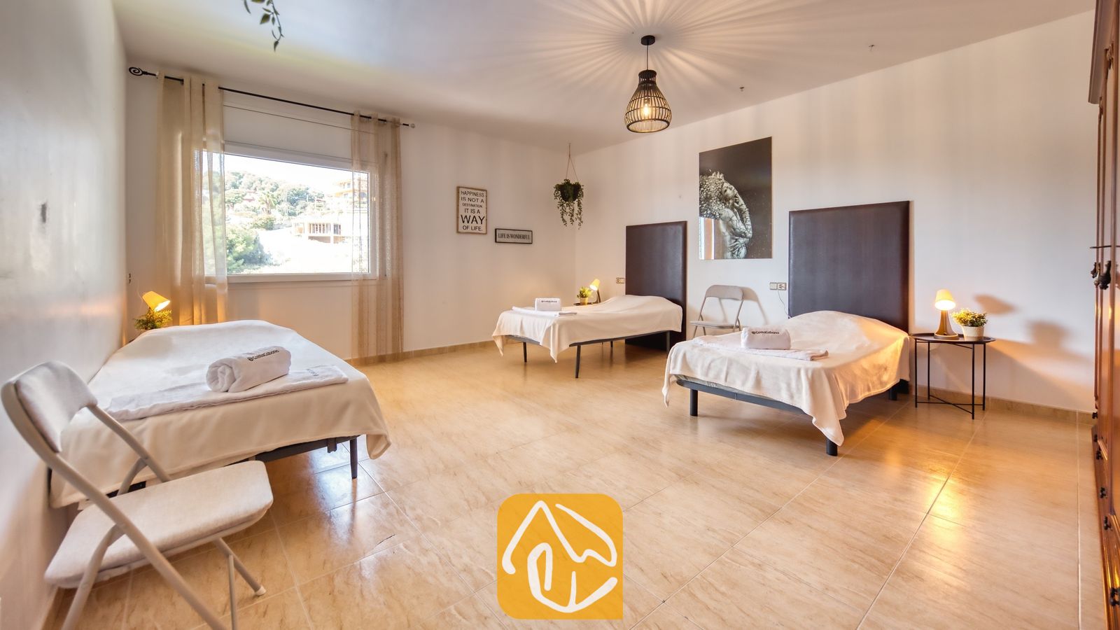 Vakantievilla's Costa Brava Spanje - Villa Marysol - Ruime slaapkamer met drie eenpersoonsbedden voorzien van donkere hoofdborden, tegelvloer en een groot raam met in-betweens.