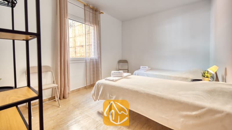 Vakantievilla's Costa Brava Spanje - Villa Marysol - Slaapkamer met twee eenpersoonsbedden, beddengoed in neutrale tinten, opgevouwen handdoeken, een klein nachtkastje en een raam met in-betweens.