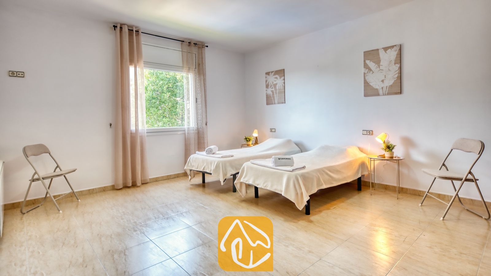 Vakantievilla's Costa Brava Spanje - Villa Marysol - Slaapkamer met twee eenpersoonsbedden, beige tegelvloeren, nachtkastjes met schemerlampen en twee klapstoelen in een witte kamer.