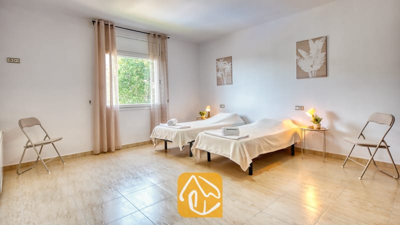 Vakantievilla's Costa Brava Spanje - Villa Marysol - Slaapkamer met twee eenpersoonsbedden, beige tegelvloeren, nachtkastjes met schemerlampen en twee klapstoelen in een witte kamer.