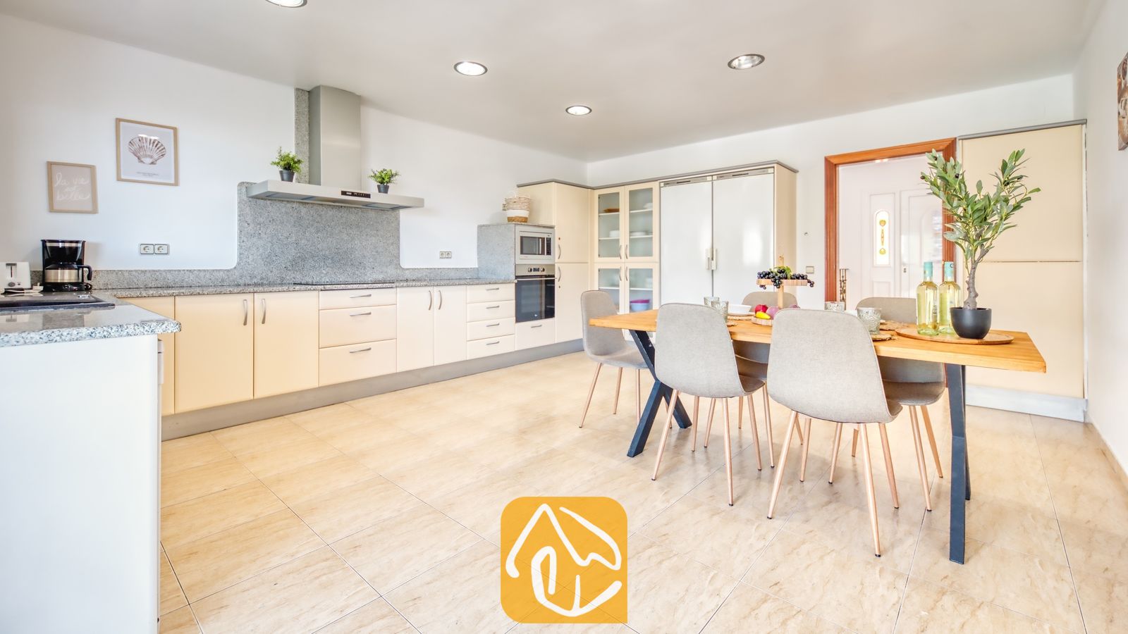 Vakantievilla's Costa Brava Spanje - Villa Marysol - Ruime open keuken en eetgedeelte in Villa Marysol, voorzien van lichtbeige kasten, granieten aanrechtbladen en een houten eettafel met grijze stoelen.