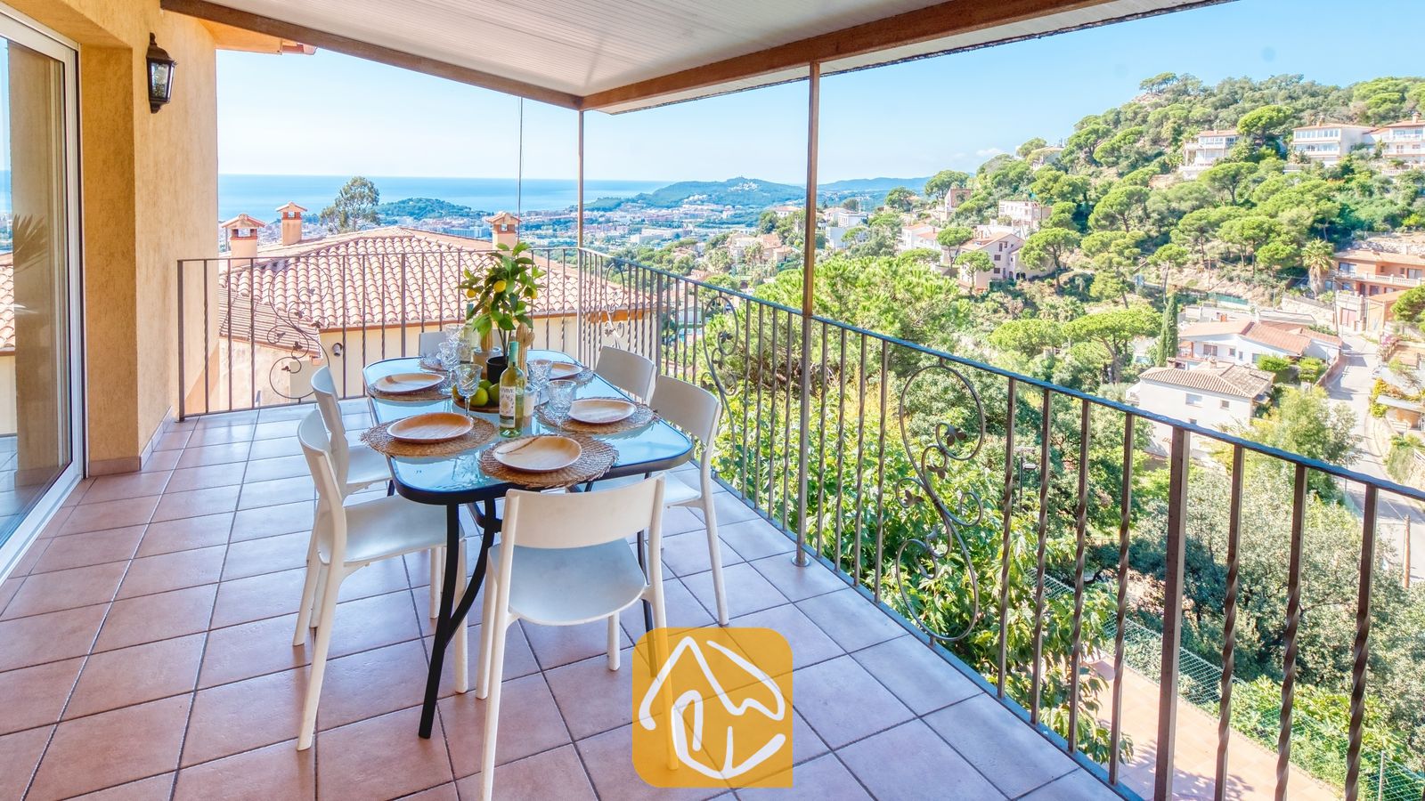 Vakantievilla's Costa Brava Spanje - Villa Marysol - Overdekt terras bij Villa Marysol met een eettafel, witte stoelen en een metalen balustrade met uitzicht op een stad en de zee.
