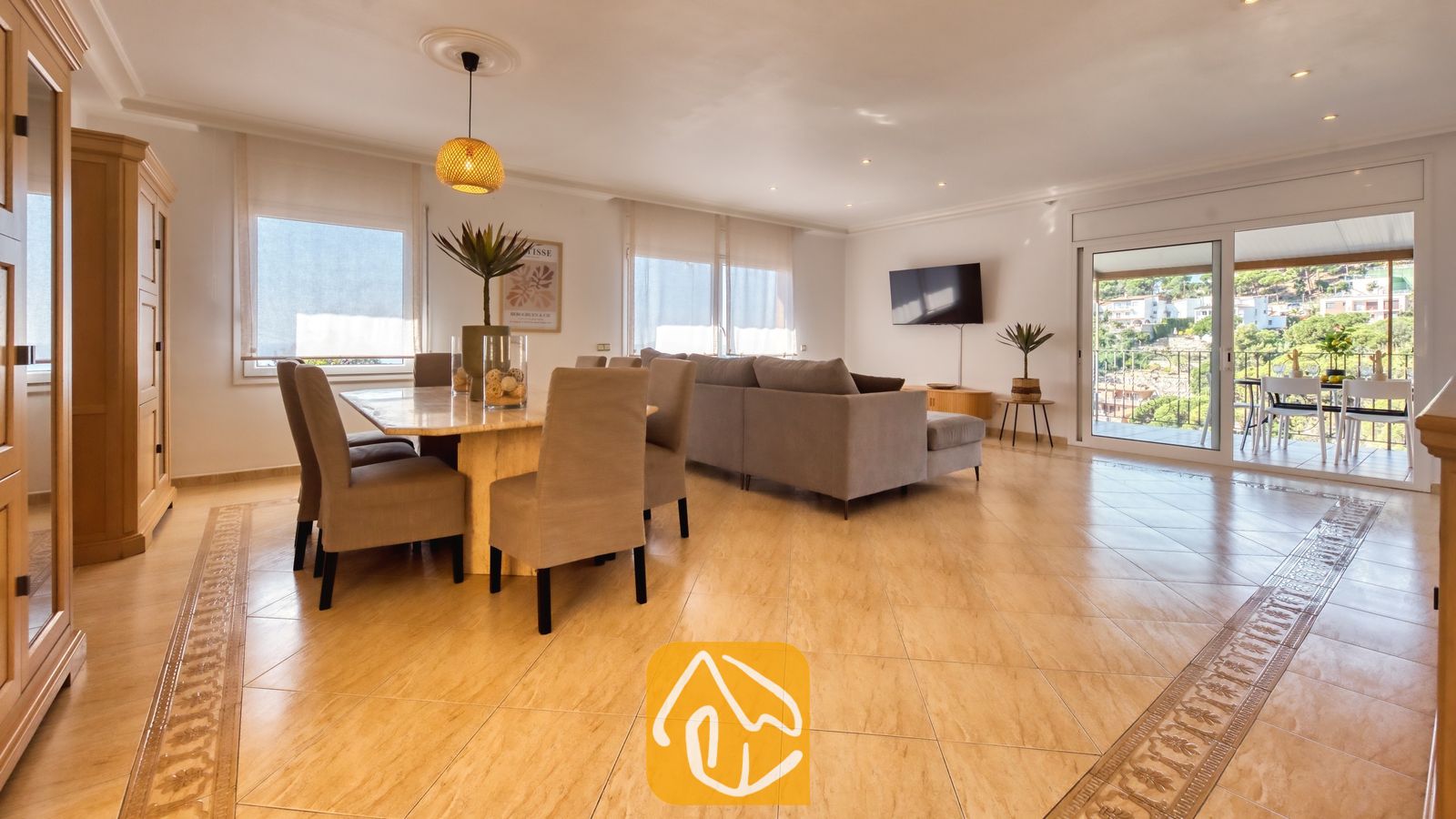 Vakantievilla's Costa Brava Spanje - Villa Marysol - Ruime woon- en eetkamer in Villa Marysol, voorzien van een marmeren eettafel, grijs gestoffeerde stoelen, een hoekbank en glazen schuifdeuren die opengaan naar een terras.