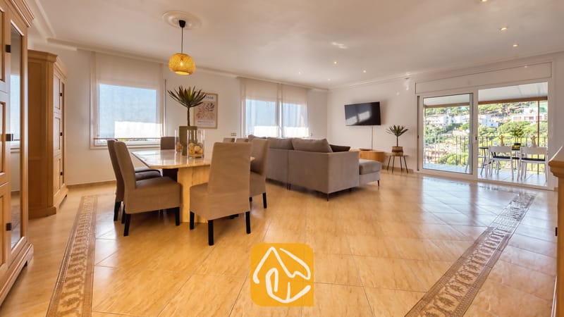 Vakantievilla's Costa Brava Spanje - Villa Marysol - Ruime woon- en eetkamer in Villa Marysol, voorzien van een marmeren eettafel, grijs gestoffeerde stoelen, een hoekbank en glazen schuifdeuren die opengaan naar een terras.