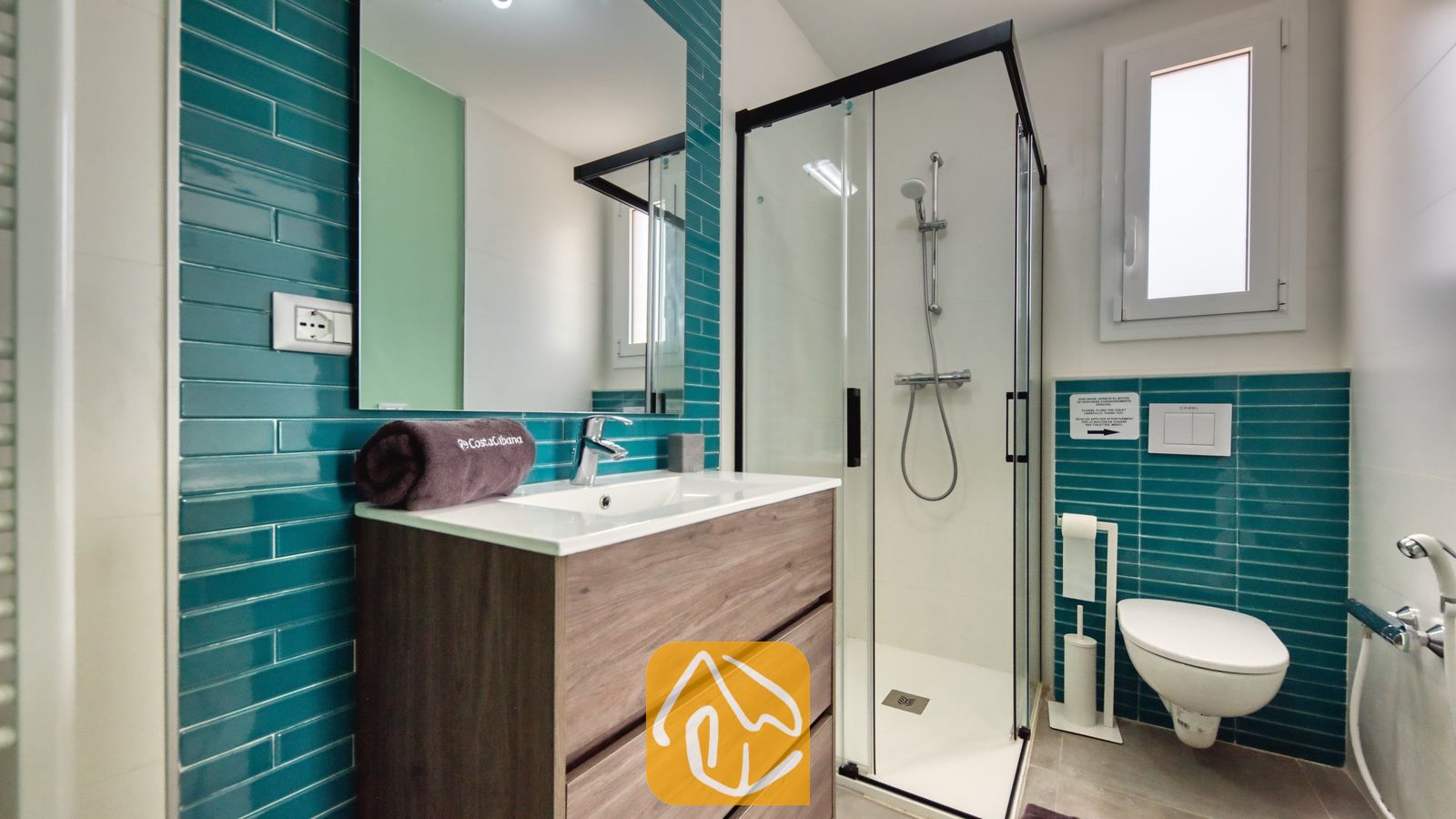 Vakantievilla's Costa Brava Spanje - Villa BellaVista - Moderne badkamer in Villa BellaVista met teal-kleurige metrotegels, een houten wastafelmeubel en een glazen inloopdouche met zwarte accenten.
