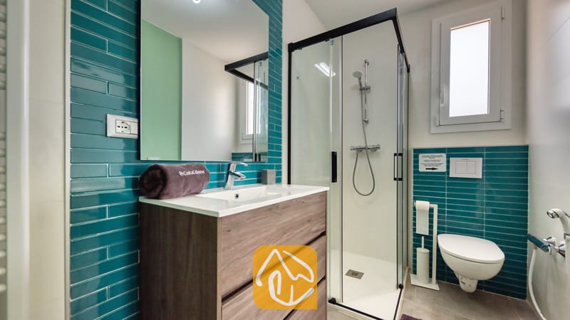 Vakantievilla's Costa Brava Spanje - Villa BellaVista - Moderne badkamer in Villa BellaVista met teal-kleurige metrotegels, een houten wastafelmeubel en een glazen inloopdouche met zwarte accenten.