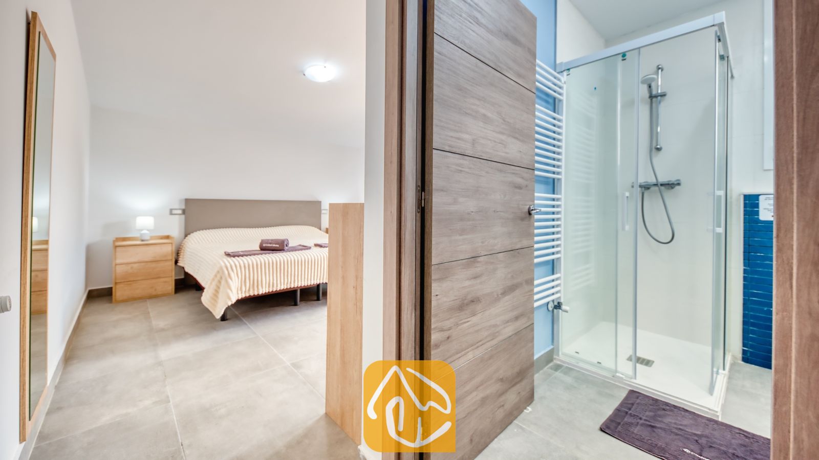 Vakantievilla's Costa Brava Spanje - Villa BellaVista - Slaapkamer en aangrenzende badkamer in Villa BellaVista, voorzien van een glazen inloopdouche, een tweepersoonsbed met beige bedlinnen en een witte designradiator.