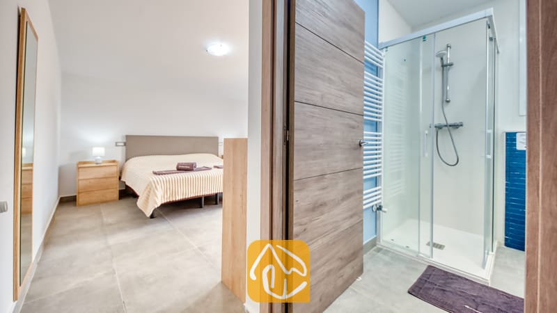 Vakantievilla's Costa Brava Spanje - Villa BellaVista - Slaapkamer en aangrenzende badkamer in Villa BellaVista, voorzien van een glazen inloopdouche, een tweepersoonsbed met beige bedlinnen en een witte designradiator.