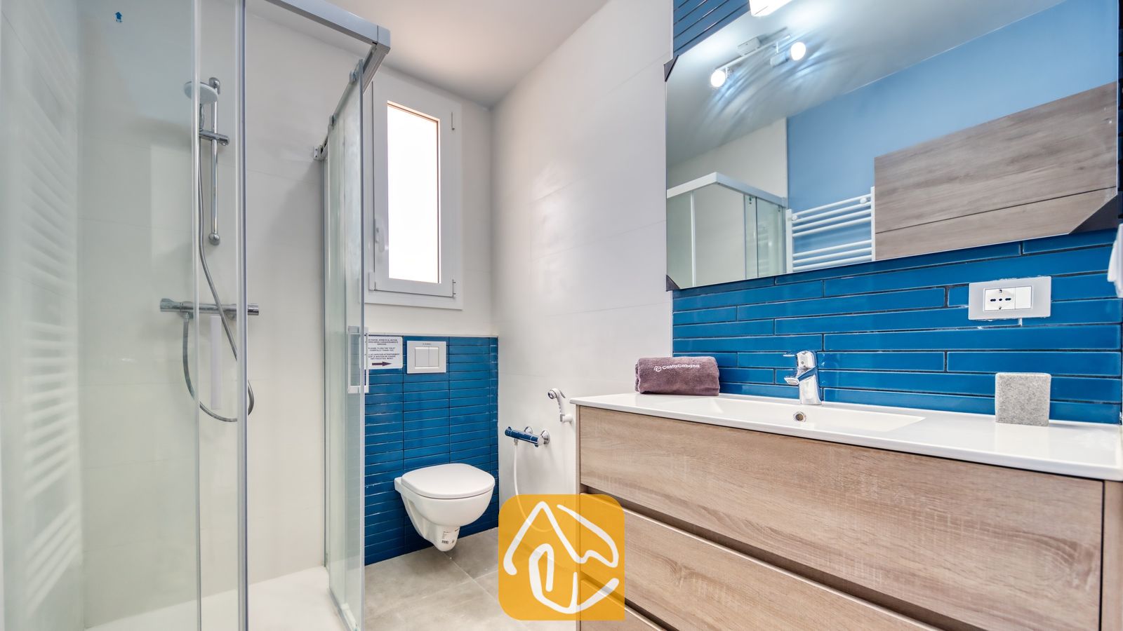 Vakantievilla's Costa Brava Spanje - Villa BellaVista - Moderne badkamer in Villa BellaVista, voorzien van een glazen inloopdouche, blauwe metrotegels en een houten wastafelmeubel met een witte waskom.