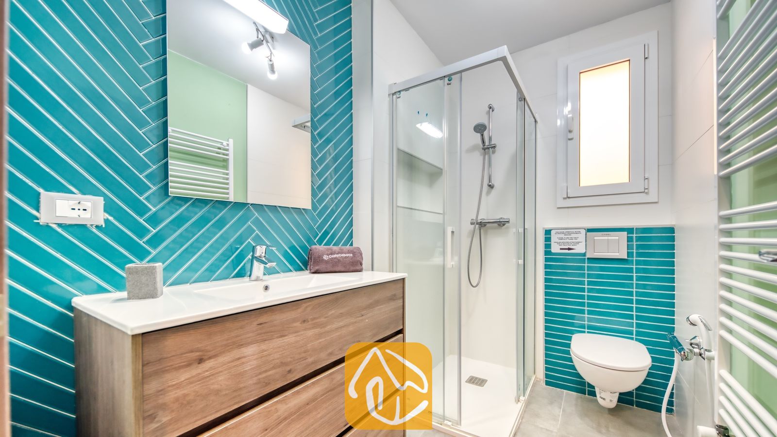 Vakantievilla's Costa Brava Spanje - Villa BellaVista - Moderne badkamer met turquoise visgraattegels, een wastafelmeubel met houtlook en een glazen douchecabine. Tevens voorzien van een hangend toilet en een witte designradiator voor handdoeken.