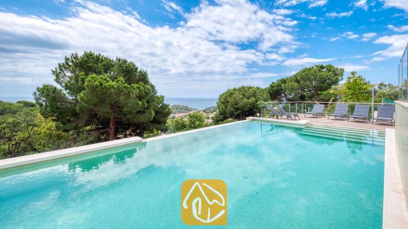 Vakantievilla's Costa Brava Spanje - Villa BellaVista - Privézwembad bij Villa BellaVista, voorzien van turkooiskleurige tegels, een zonneterras met glazen omheining en grijze ligbedden, met uitzicht op de zee en de dennenbomen.
