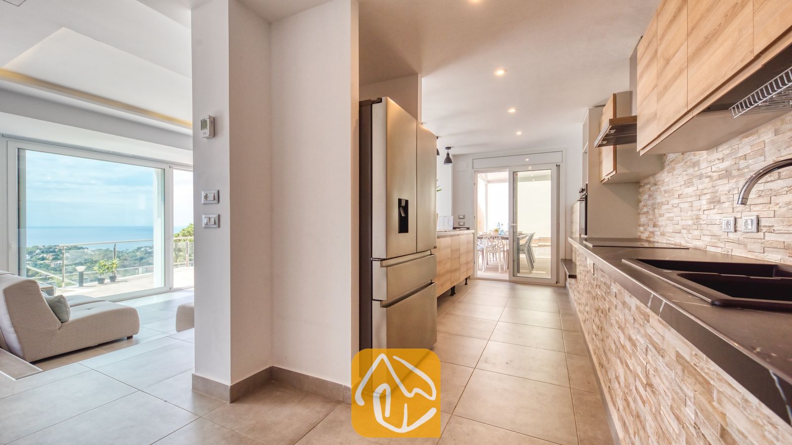 Vakantievilla's Costa Brava Spanje - Villa BellaVista - Moderne keuken in Villa BellaVista, voorzien van een roestvrijstalen koelkast, lichthouten kasten en een achterwand met steenstructuur, die uitkomt op een terras met