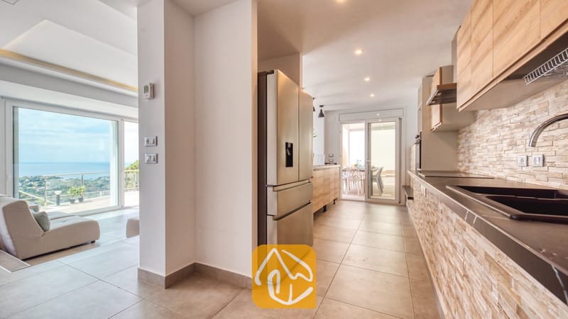 Vakantievilla's Costa Brava Spanje - Villa BellaVista - Moderne keuken in Villa BellaVista, voorzien van een roestvrijstalen koelkast, lichthouten kasten en een achterwand met steenstructuur, die uitkomt op een terras met