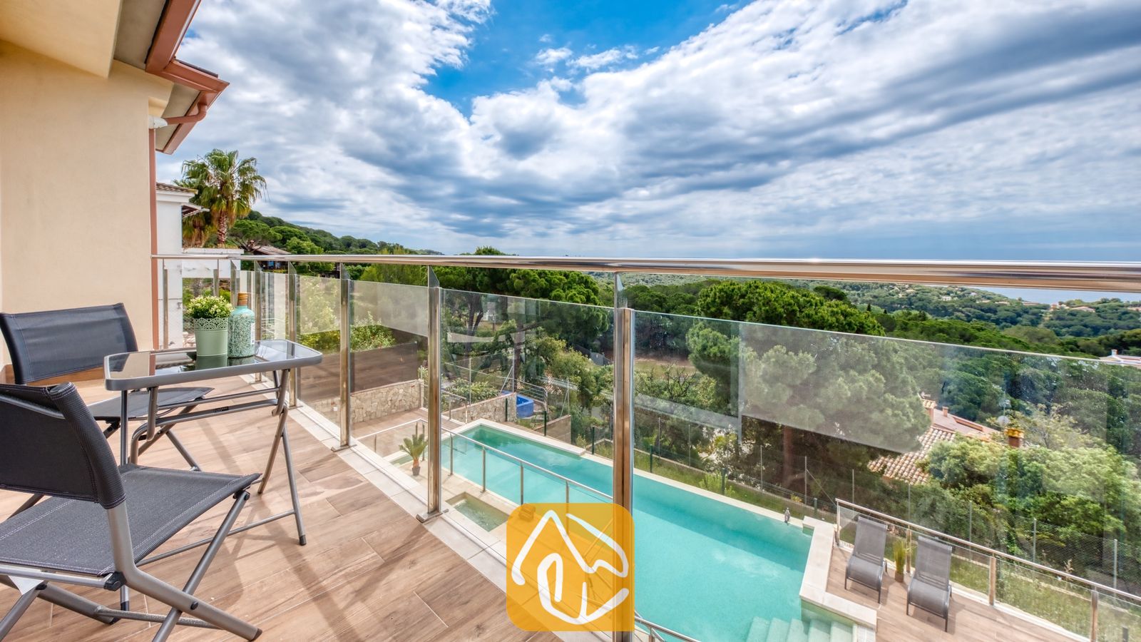 Vakantievilla's Costa Brava Spanje - Villa BellaVista - Terras van Villa BellaVista met glazen balustrades en uitzicht op een rechthoekig zwembad, voorzien van zwarte klapstoelen en een klein tafeltje op tegels met houtlook.