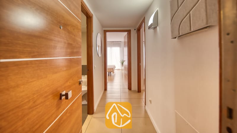 Vakantievilla's Costa Brava Spanje - Apartment Gaudi - De binnenhal van Appartement Gaudi, voorzien van witte muren, tegelvloeren en houten deuren die leiden naar een helder verlichte slaapkamer.