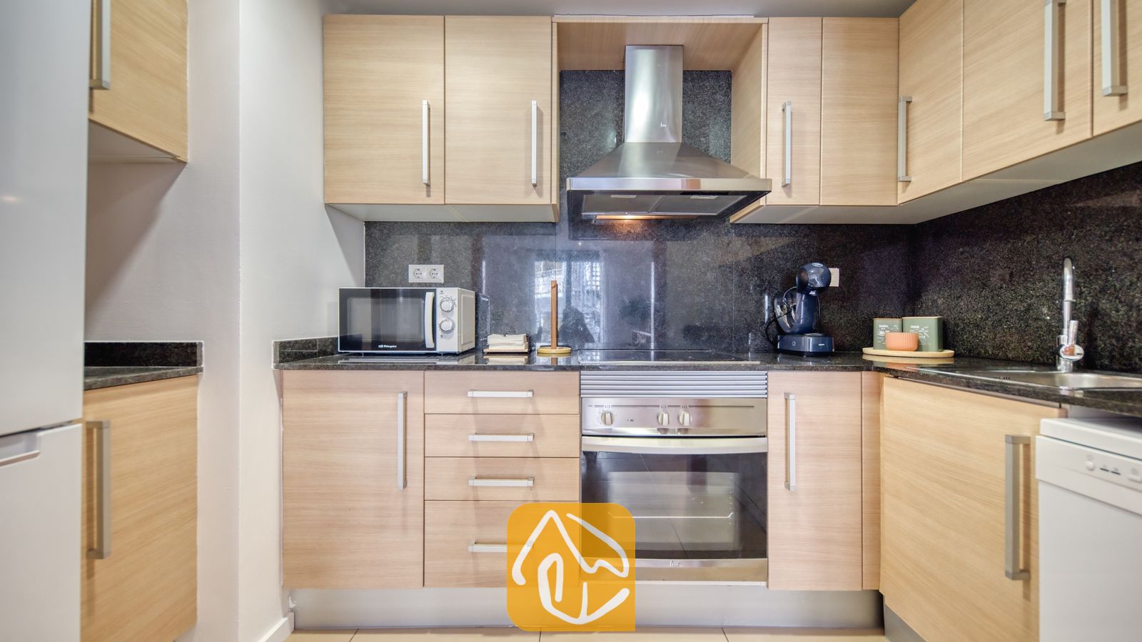 Vakantievilla's Costa Brava Spanje - Apartment Gaudi - Keuken met licht houten kasten, donkere granieten aanrechtbladen, een roestvrijstalen oven en een bijpassende afzuigkap